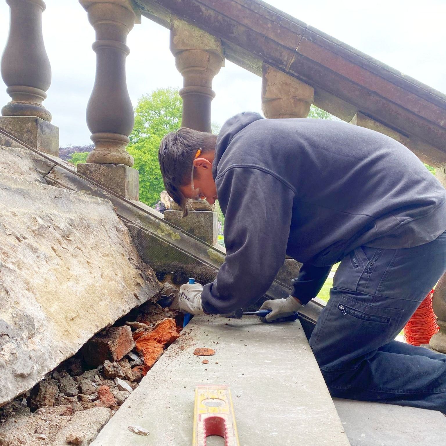 A man is kneeling down next to a level while working on a staircase repair.