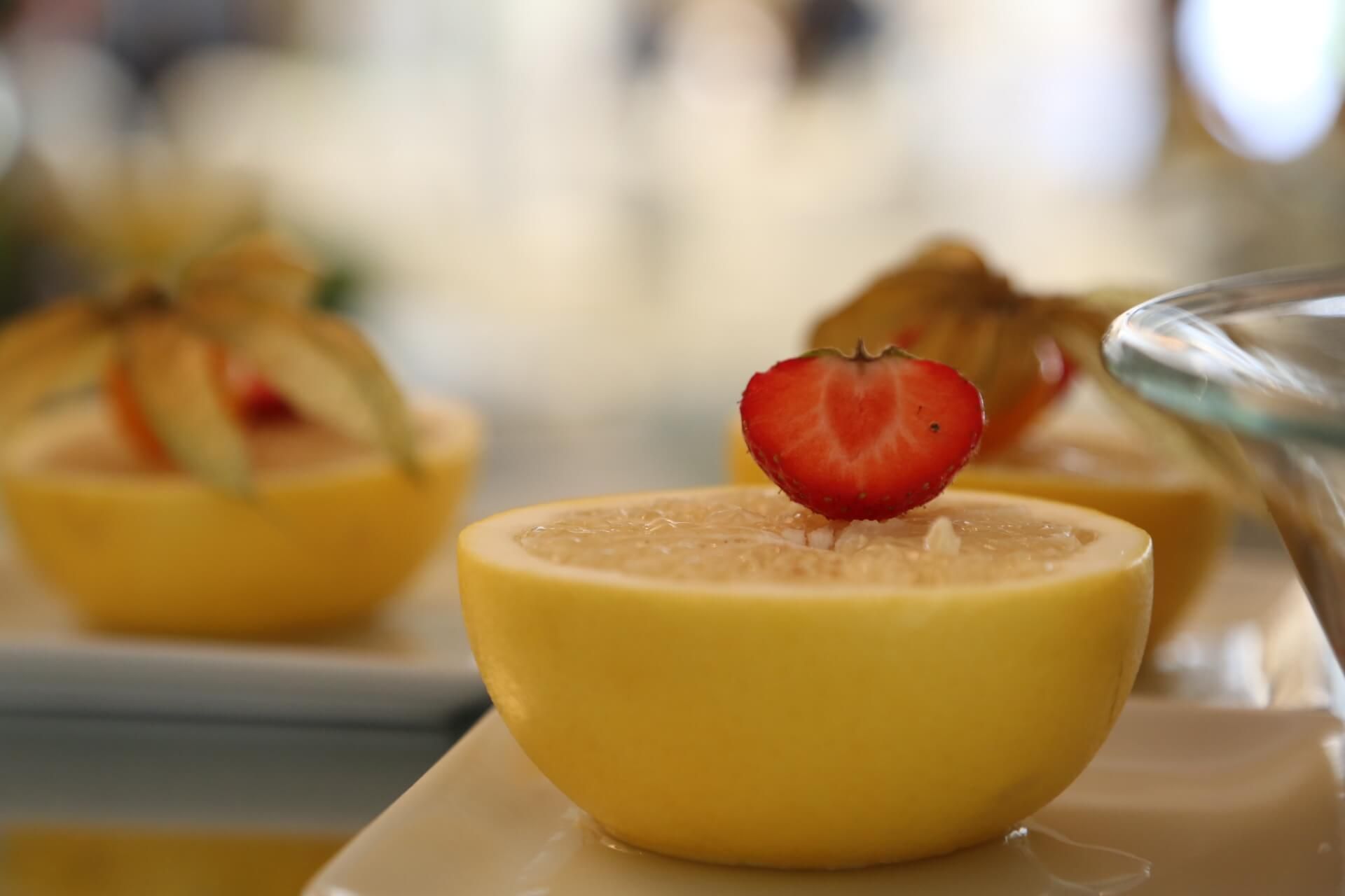 Half lemons filled with yellow pulp, topped with a strawberry half on a white plate.