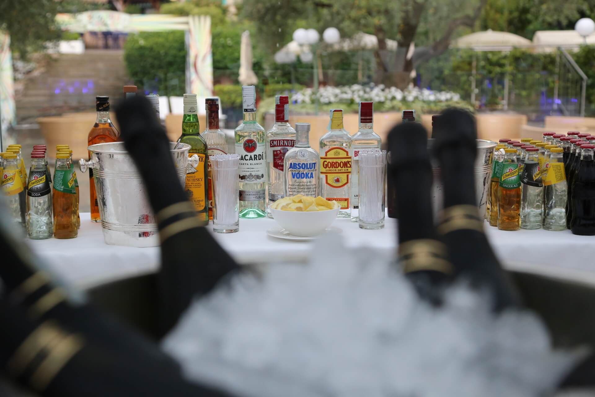 Bar setup with various liquor bottles, champagne in an ice bucket, and snacks on a white table.
