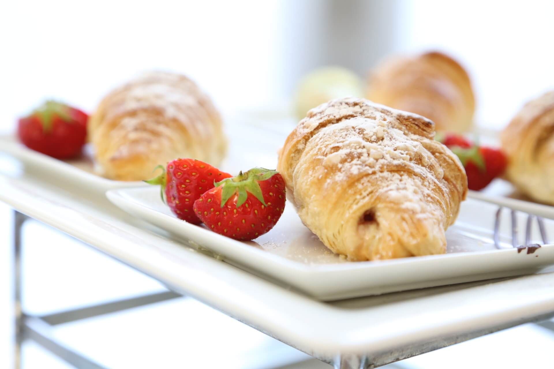 Croissants dusted with powdered sugar and fresh strawberries on white platters.