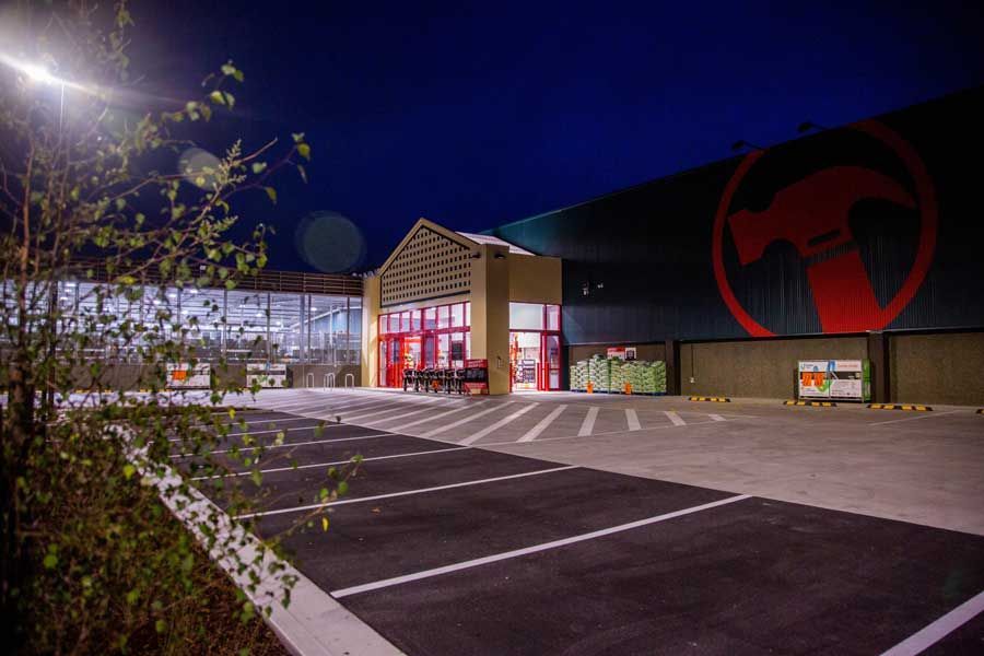 Exterior of a hardware store at night with bright signage and empty parking lot.