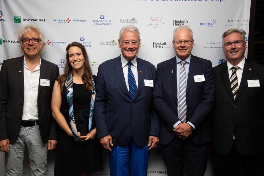 Five people in formal attire pose in front of a backdrop with logos.