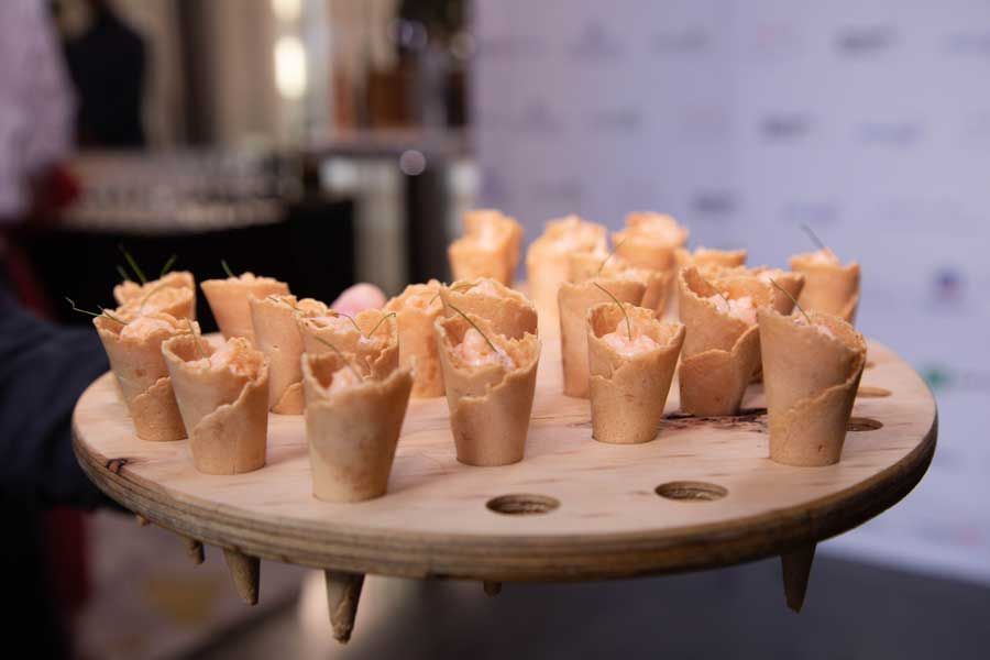 Tray of small appetizers in cone-shaped cups, filled with pink cream, topped with chives.