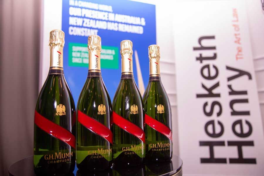 Four bottles of G.H. Mumm champagne with red ribbon, near a sign for Hesketh Henry law firm.