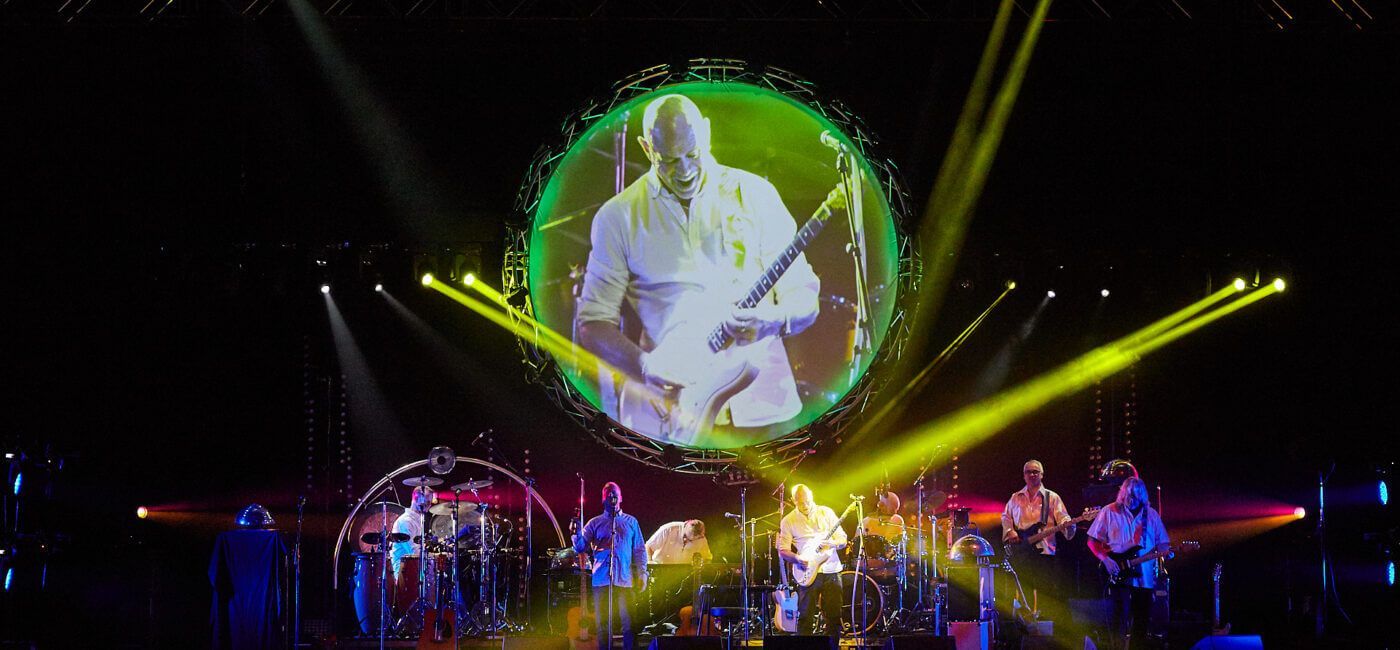 Pink Floyd Experience Concert with a guitarist on a large screen. Band playing on stage, stage lights.