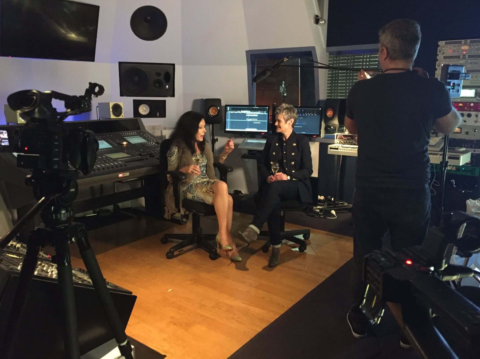 Two women are being interviewed in a recording studio. A camera and a crew member are also present.