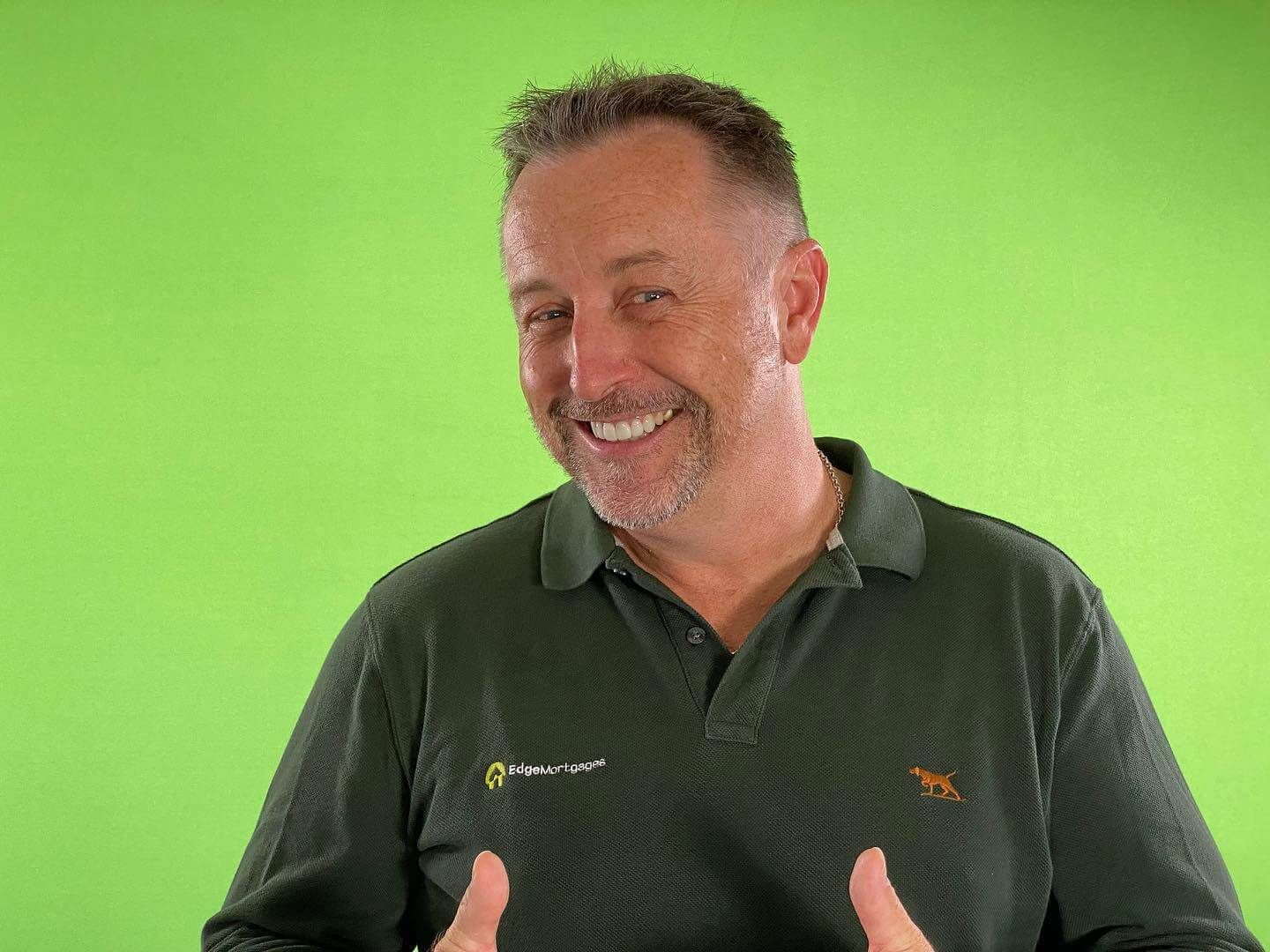 Man in green shirt smiles and gives thumbs-up in front of a green screen.