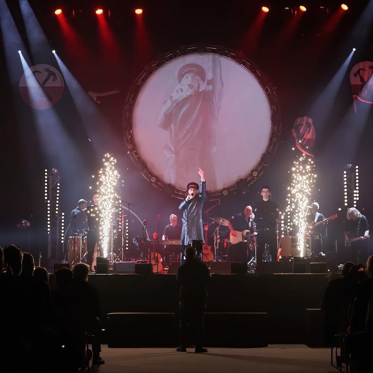 Singer on stage with band, performing in front of a large screen, pyrotechnics, and a crowd for the Pink Floyd Experience 