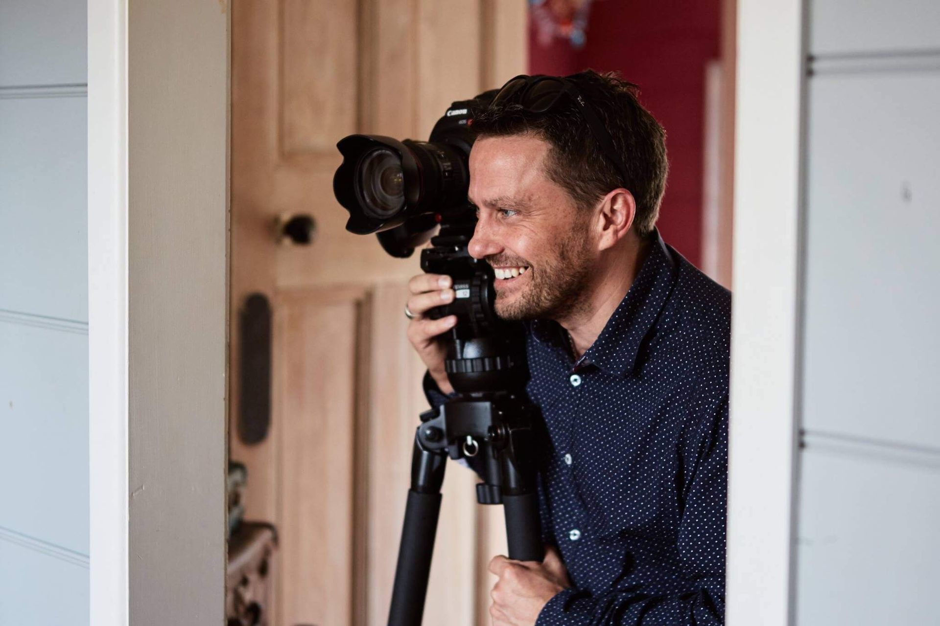 Craig Walsh with camera on tripod, smiling, photographing from a doorway.