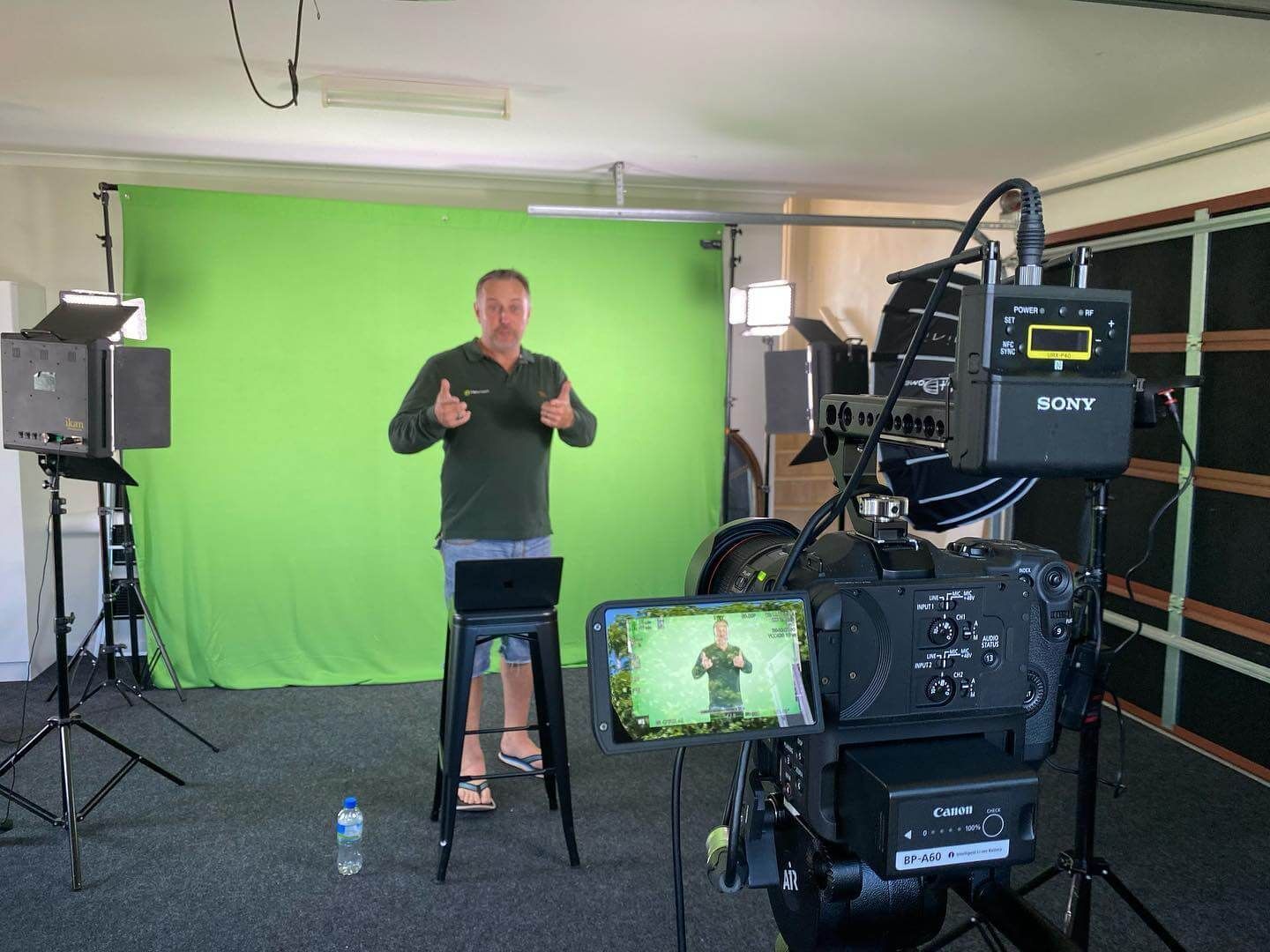 Man standing in front of a green screen, filming with a professional camera; he gives two thumbs up.