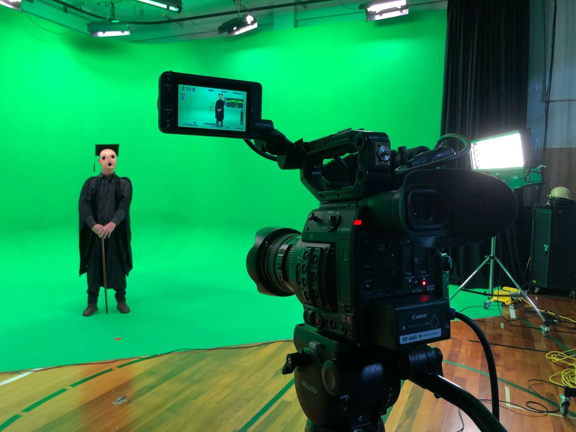 Camera filming a person in a dark coat posing in front of a green screen.