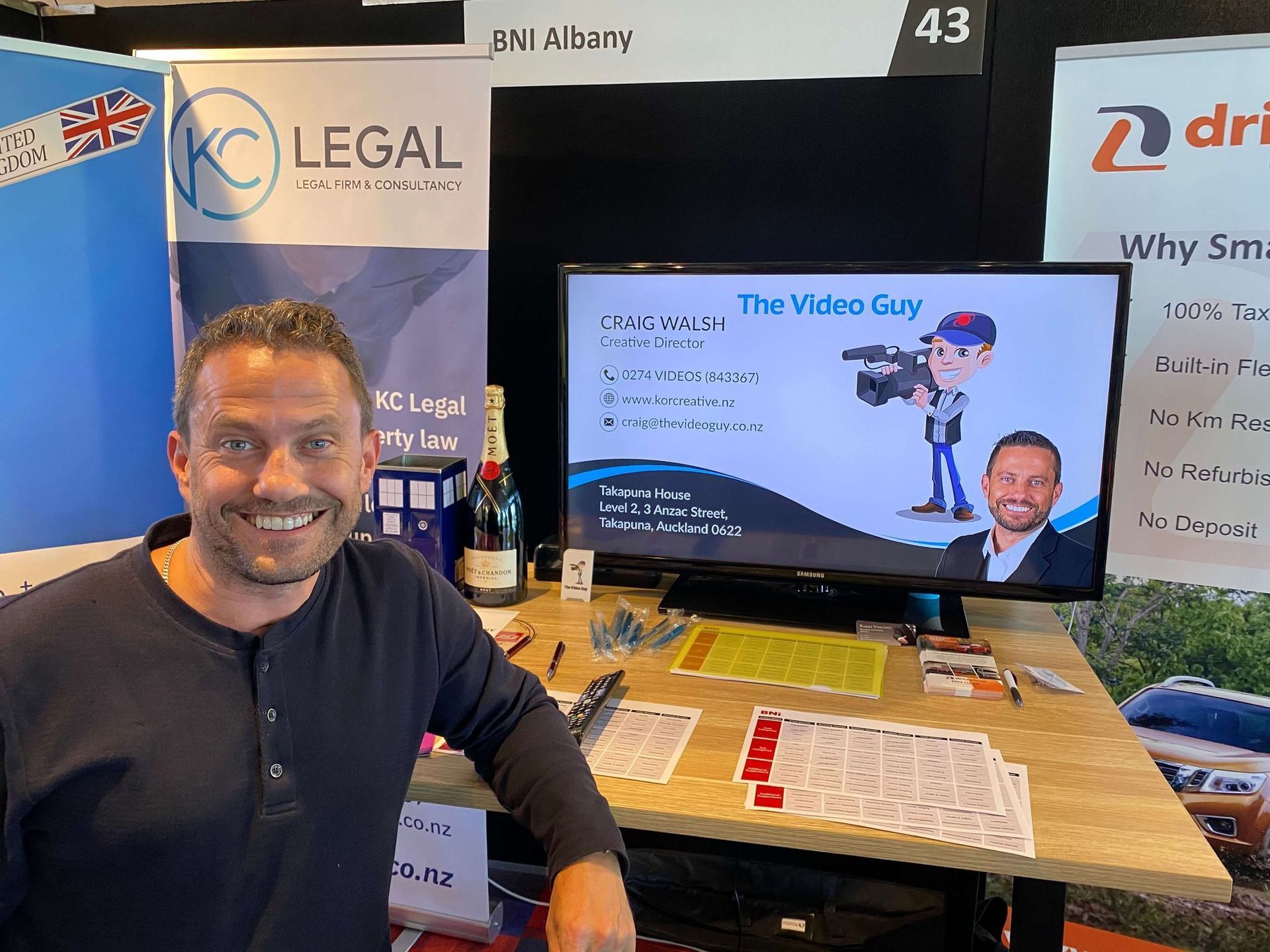 Man smiling at camera, standing at a trade show booth for 