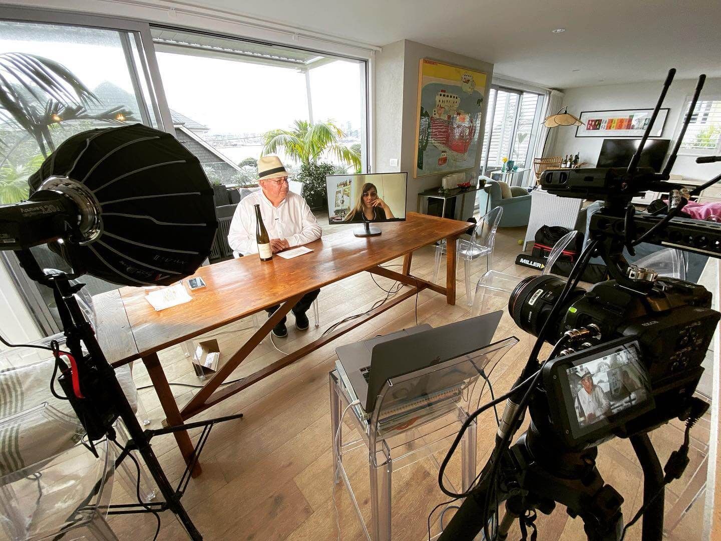 Man seated at table being filmed in a brightly lit room. A camera and lights are set up.
