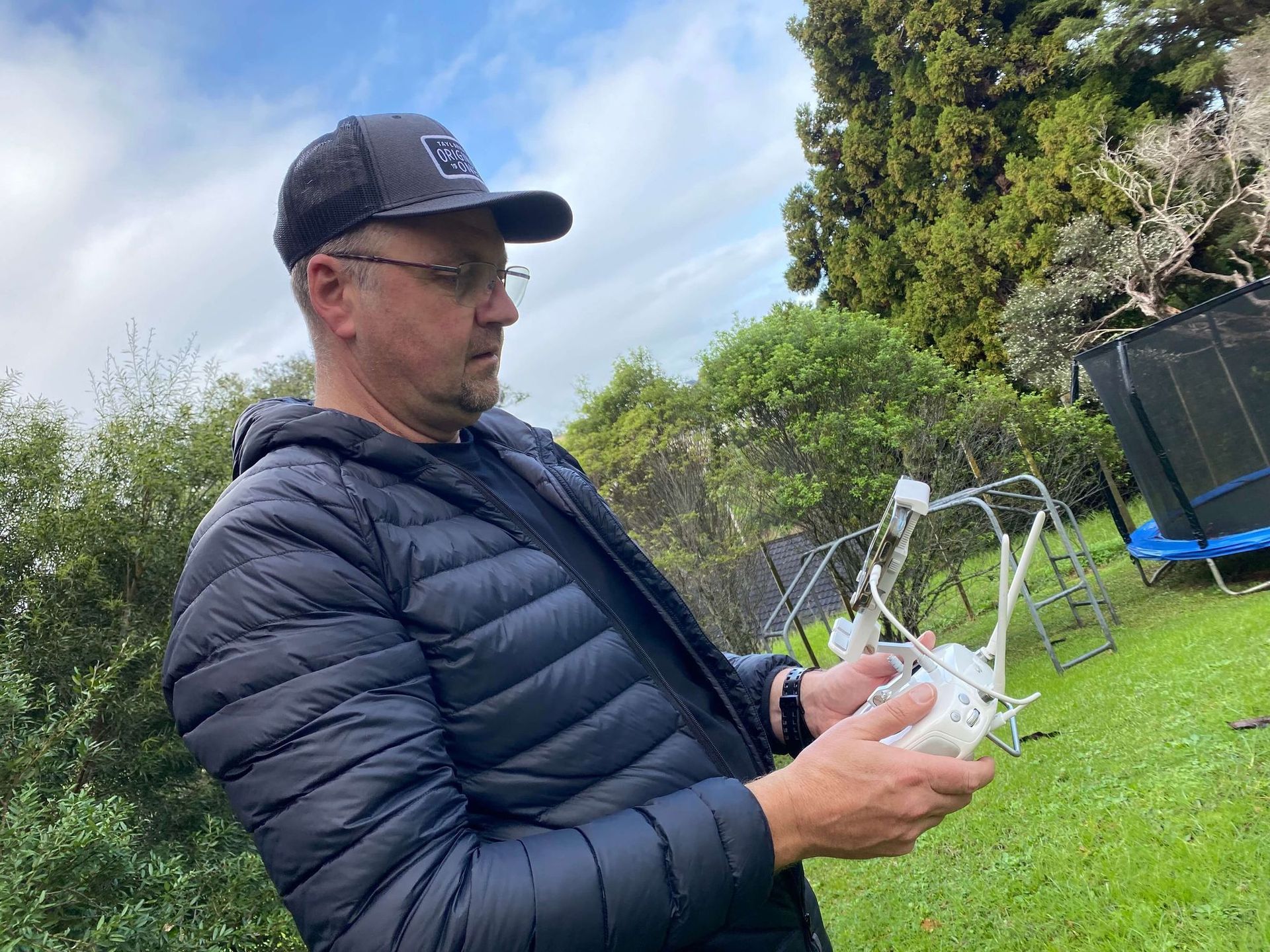 Man in cap operates drone controller for Monster Wash outdoors in grassy yard.