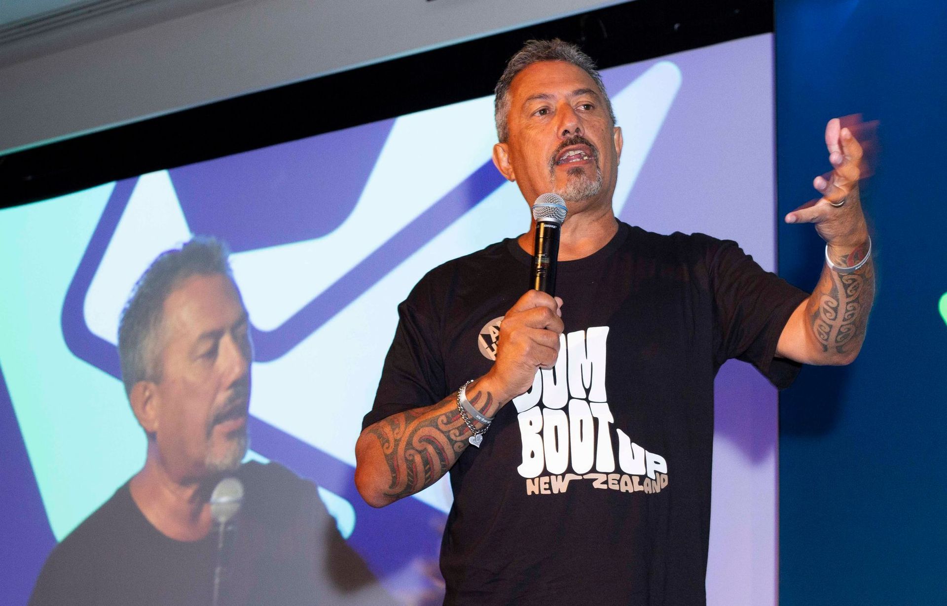 Mike King speaking into microphone on stage with projection screen.