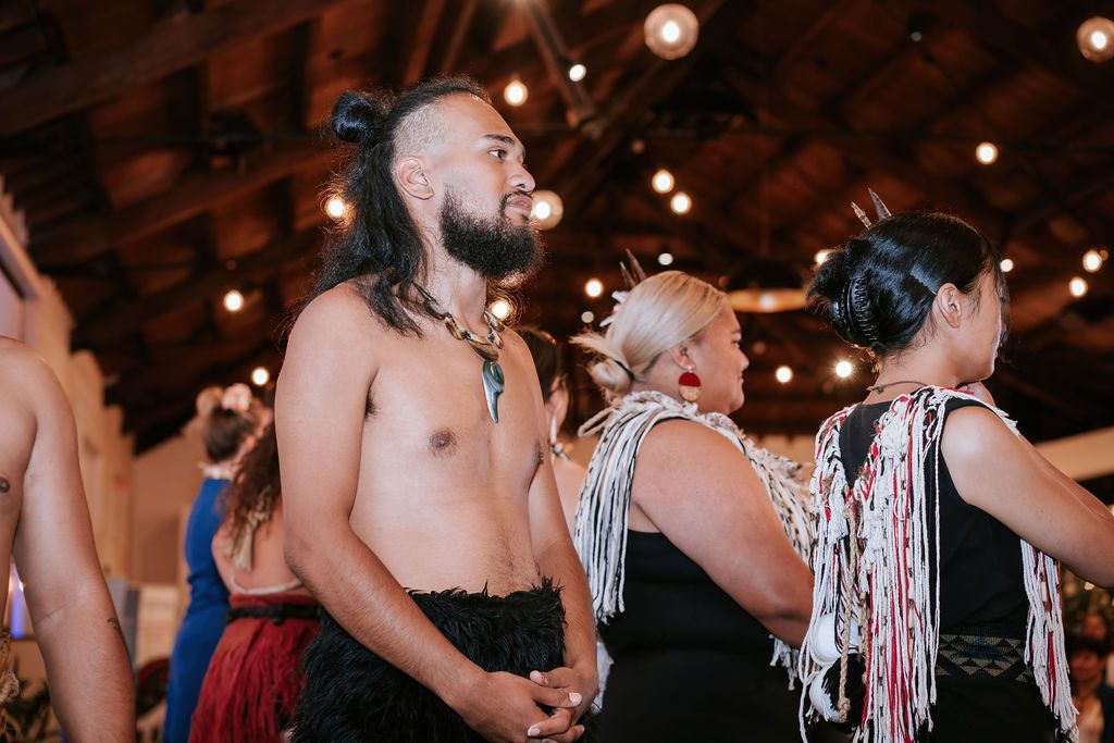Group of people, some bare-chested, performing a cultural dance indoors.