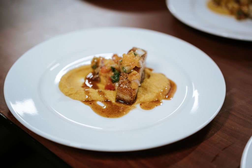 A plated dish of food with a rectangular piece of meat, sauce, and a yellow puree on a white plate.