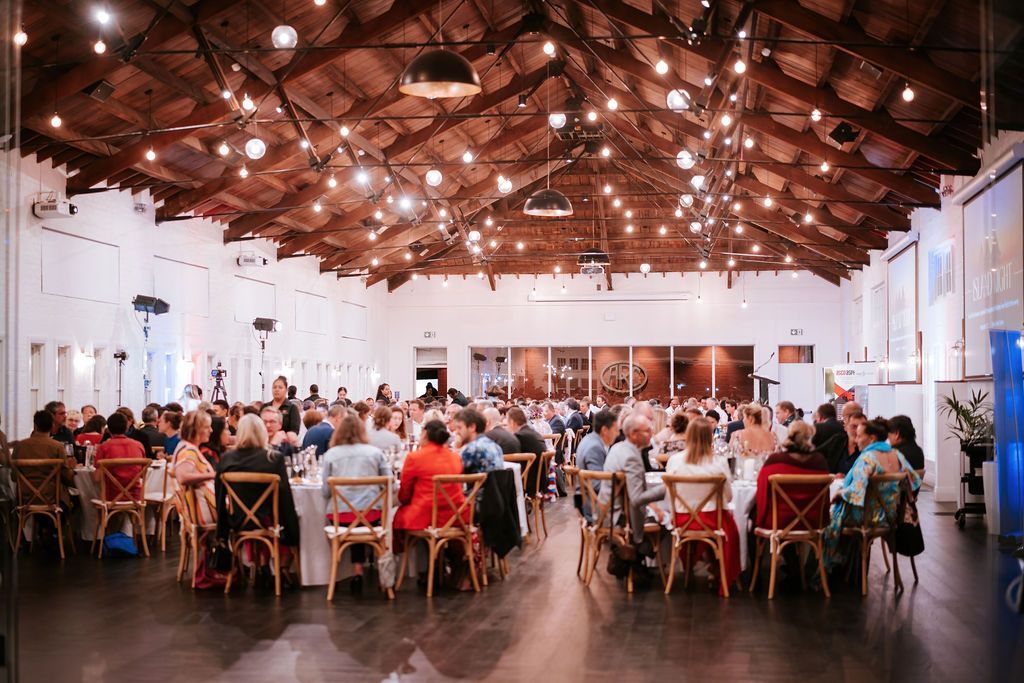 Large event space with people seated at tables, under string lights.