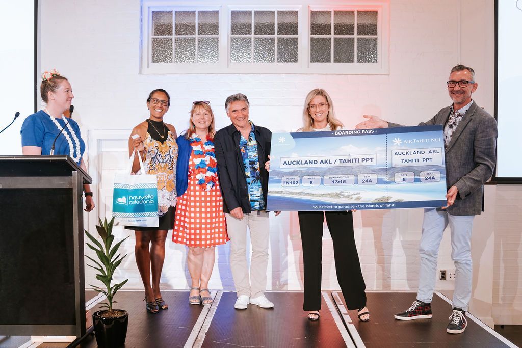 People holding a large check onstage at an event. They are standing on a stage with a screen and plants.