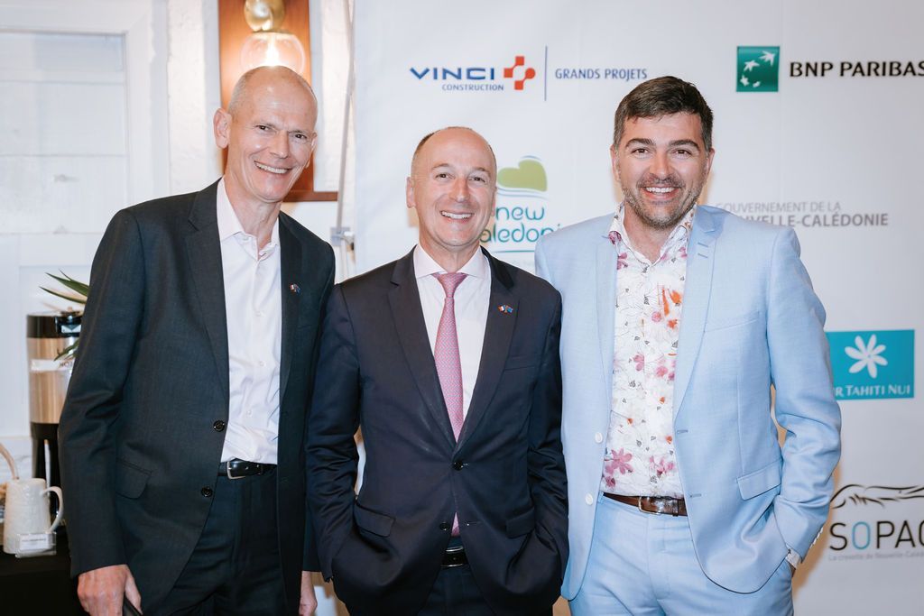 Three men in suits pose together at an event.