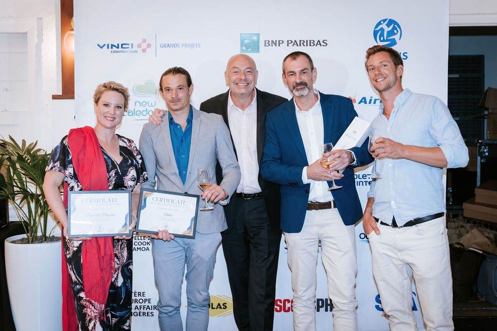 Group of people holding awards, smiling near a logo wall, inside a well-lit event.
