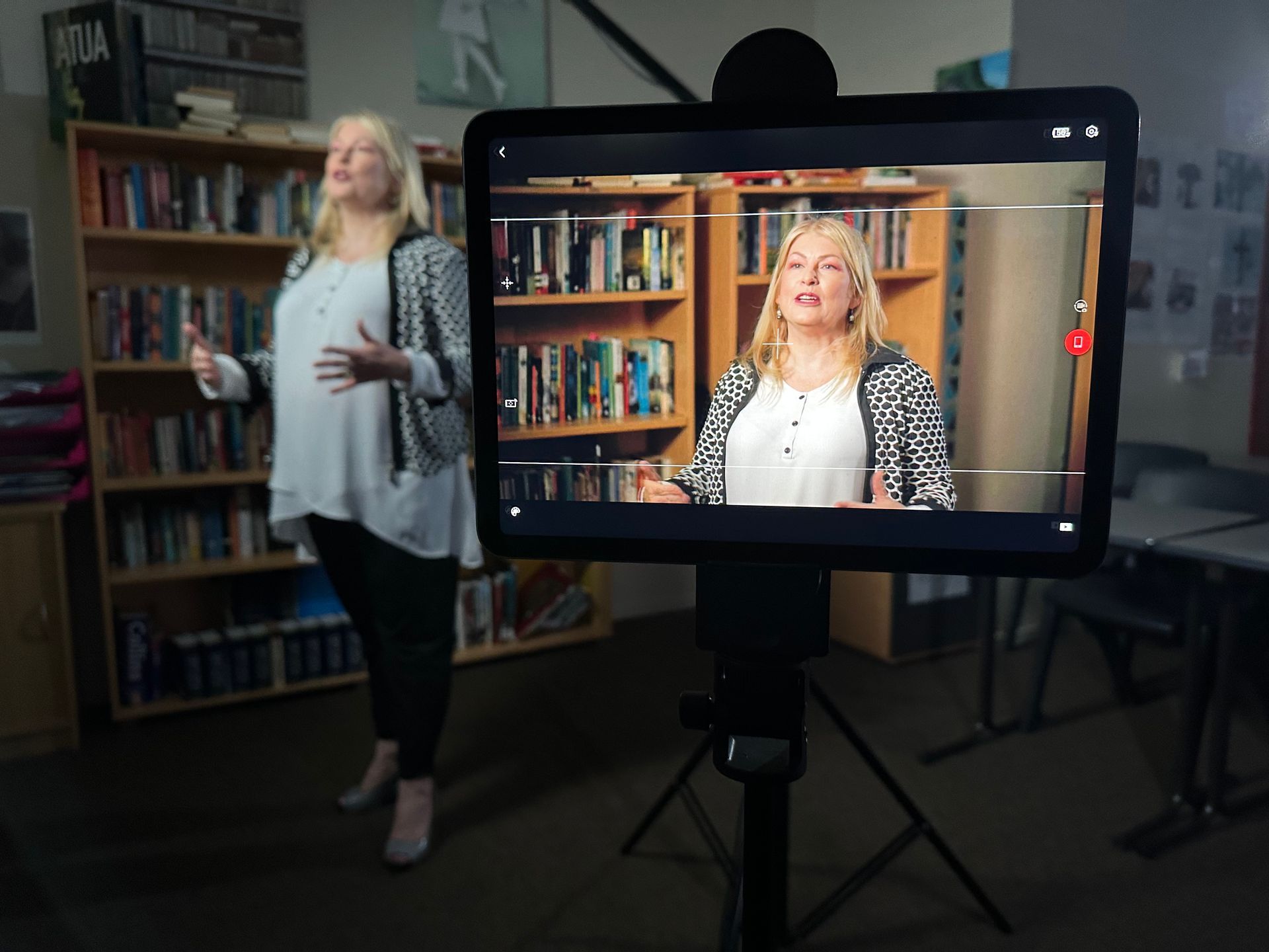 Woman in front of a screen displaying her image, standing in a library.