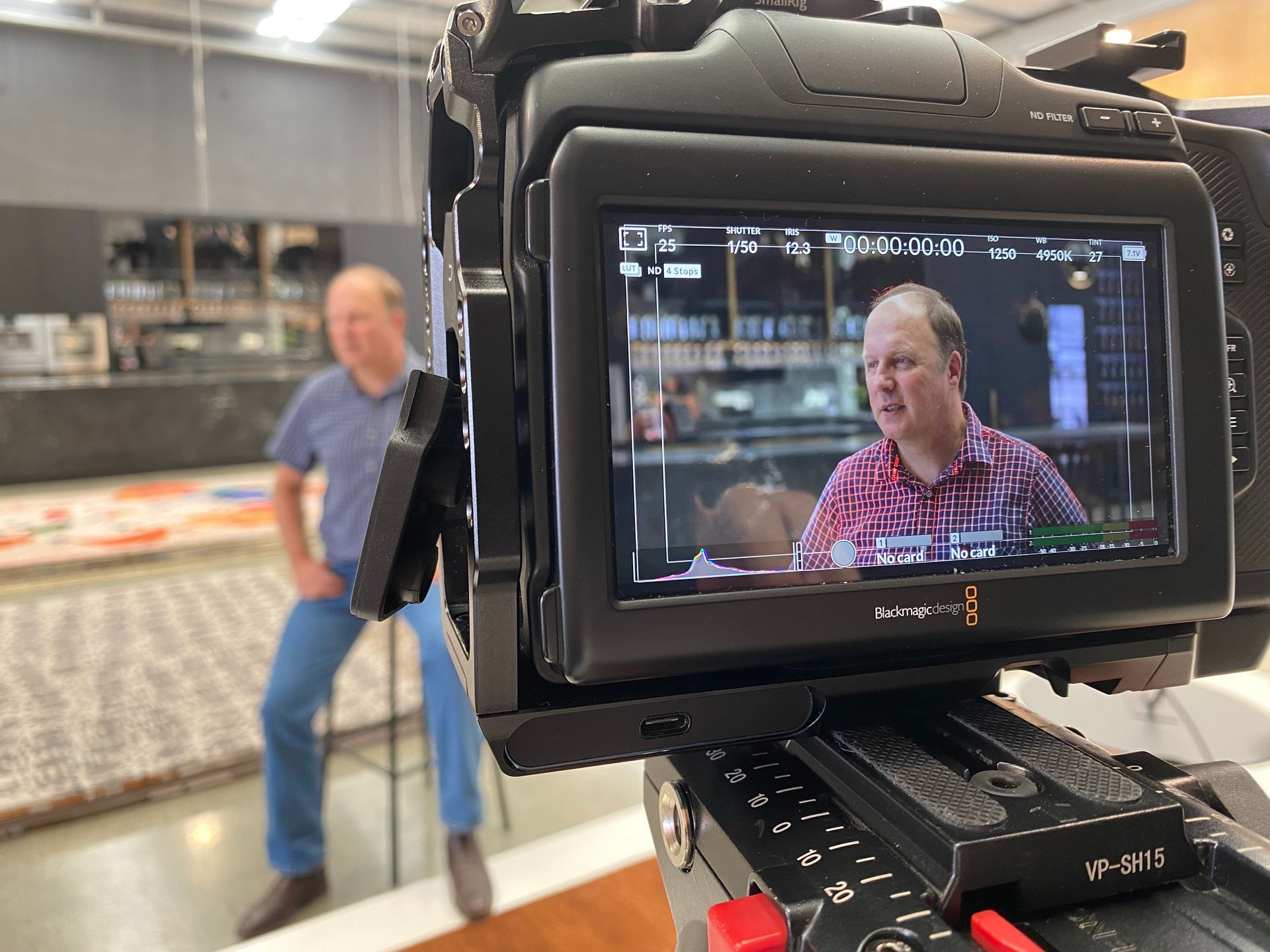 A person being filmed with a camera. The camera's screen shows the person being interviewed indoors.