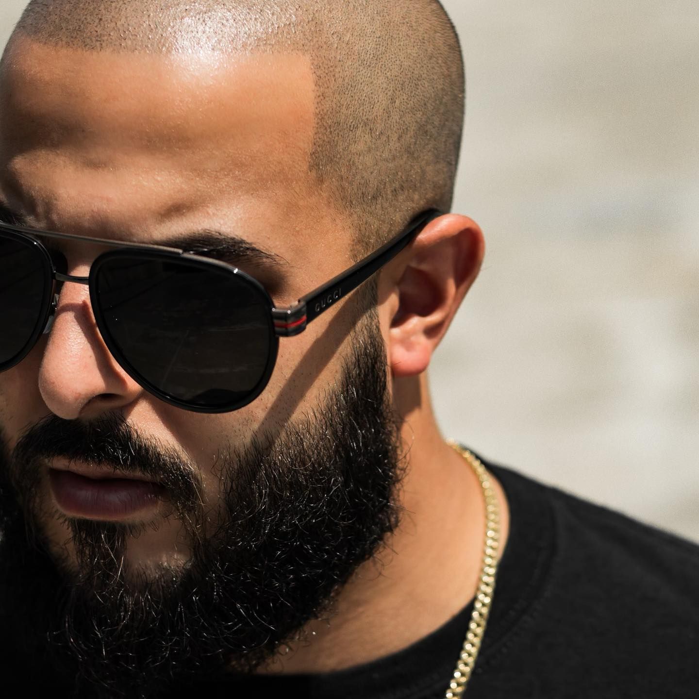 A man with a beard wearing sunglasses and a chain around his neck