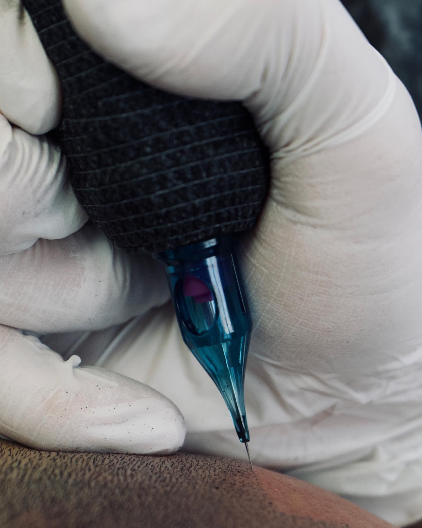 A person wearing white gloves is holding a blue tattoo machine
