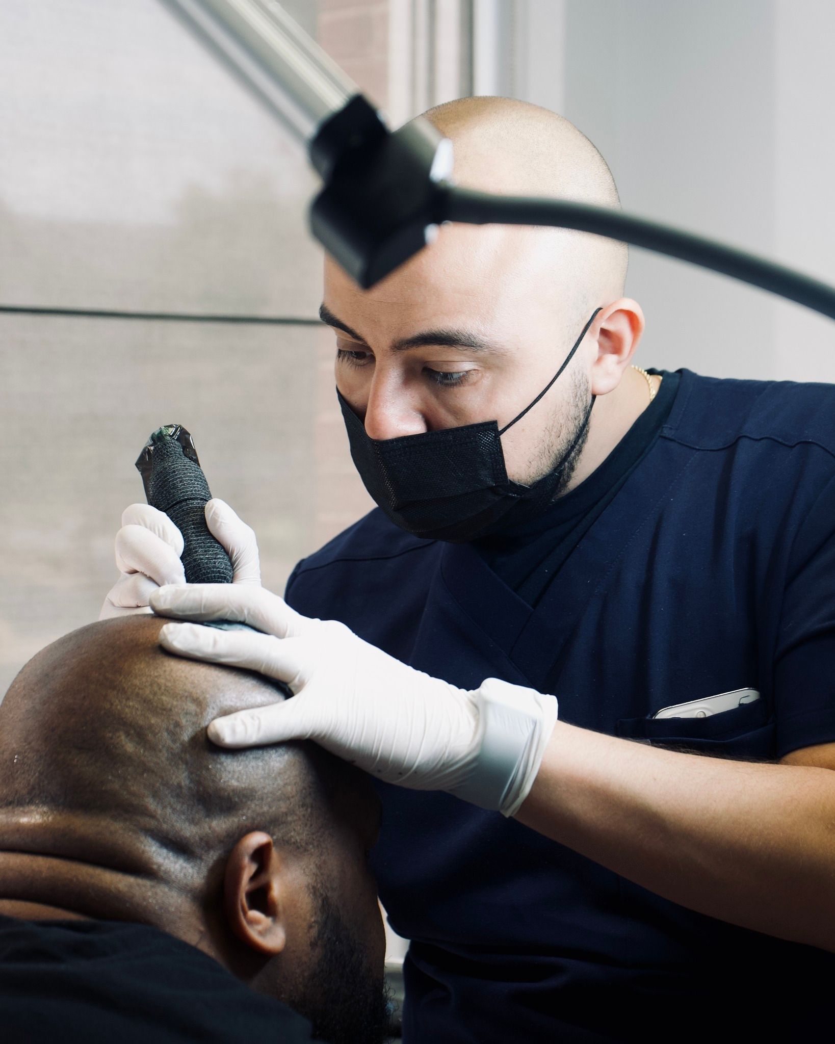 A man wearing a mask and gloves is working on a bald man 's head.