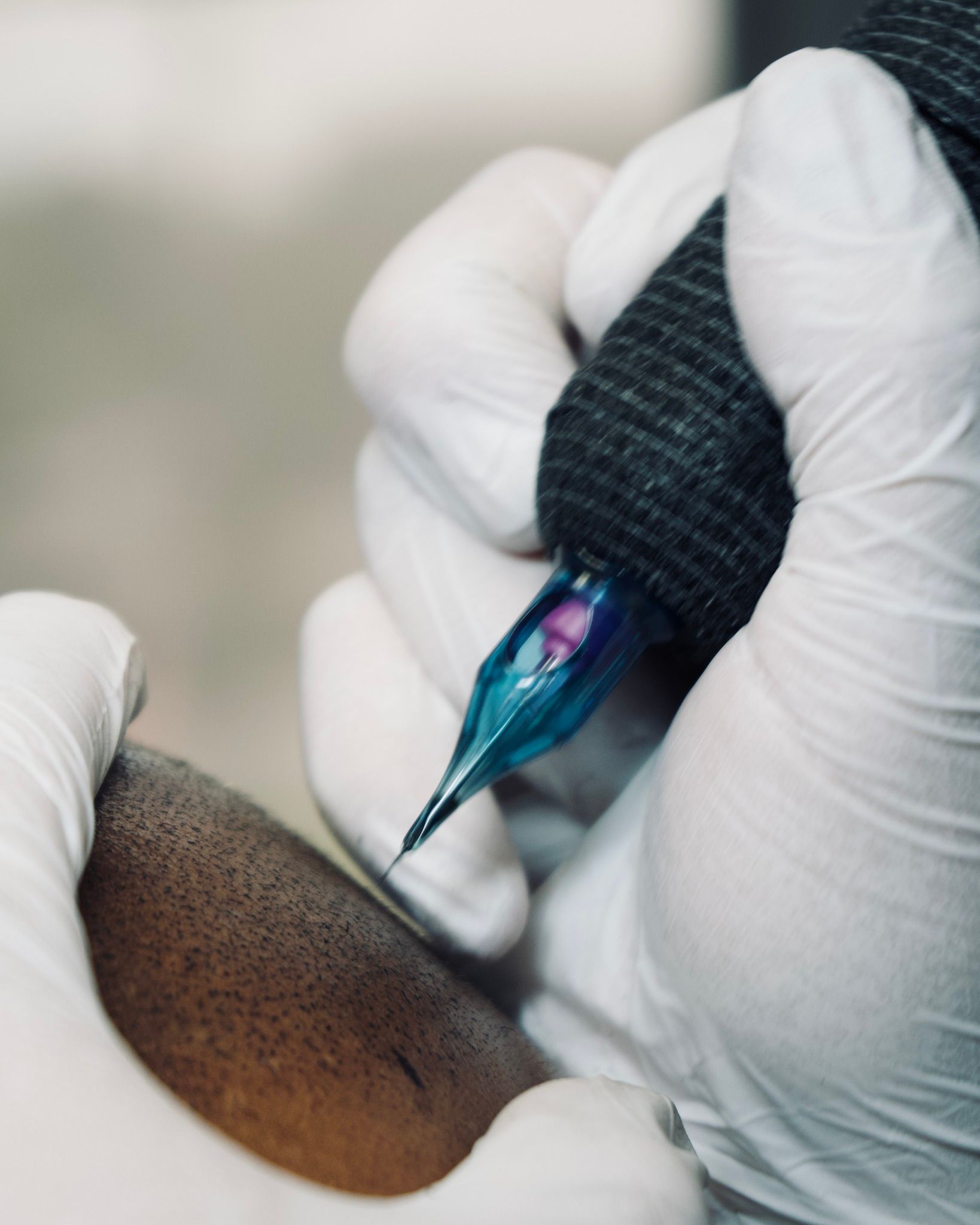 A person wearing white gloves is holding a tattoo machine