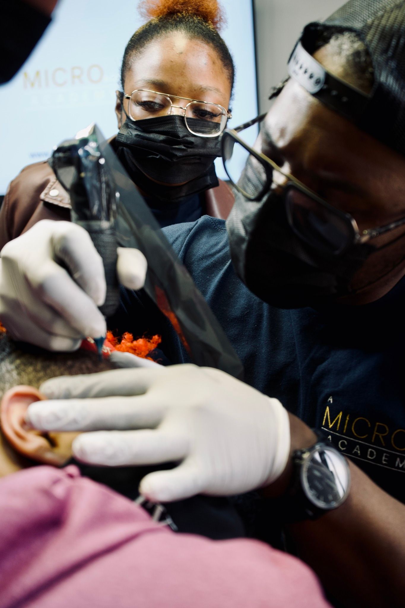 A man is getting a tattoo on a woman 's ear.