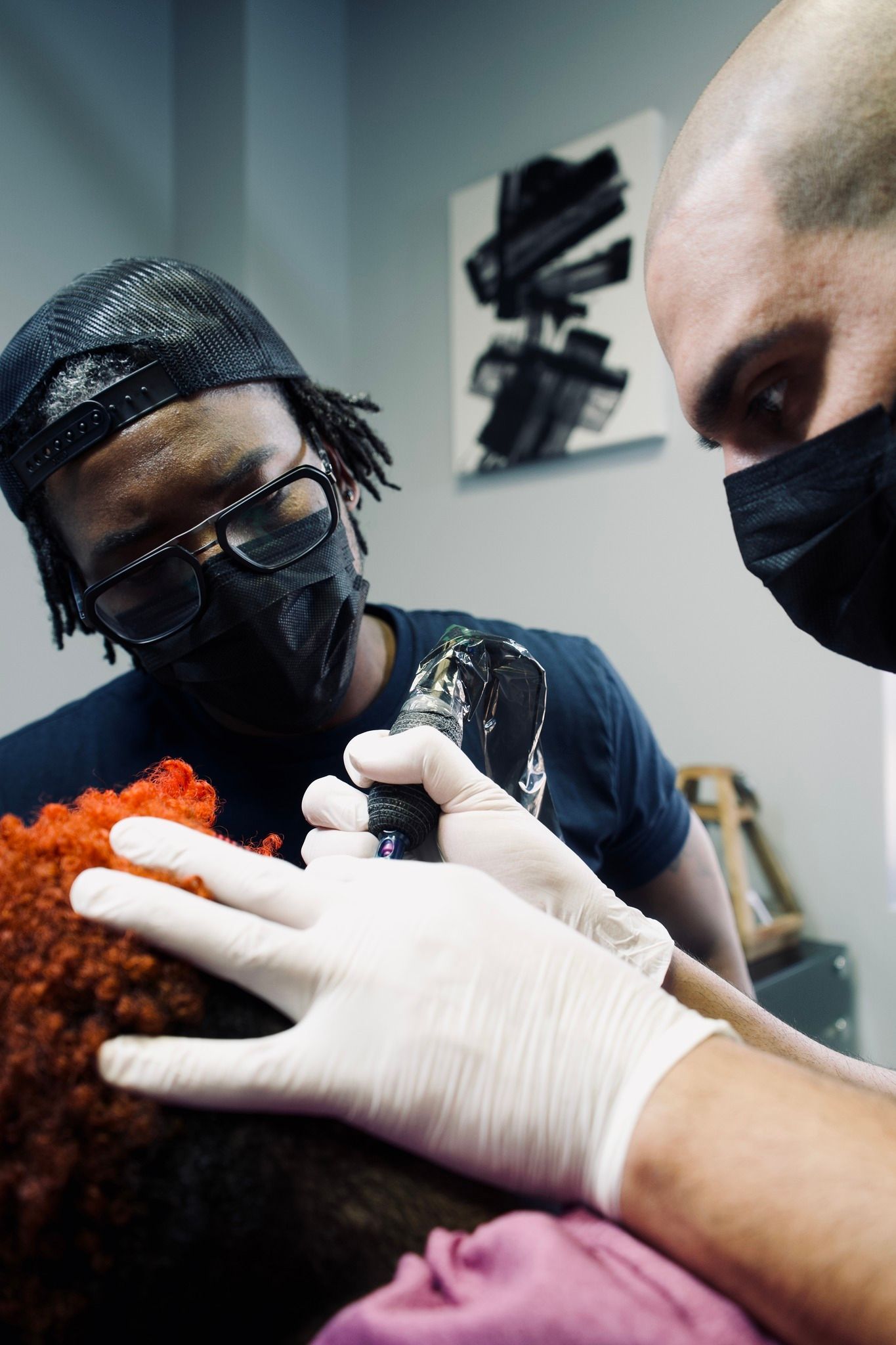 Two men wearing masks and gloves are getting a tattoo