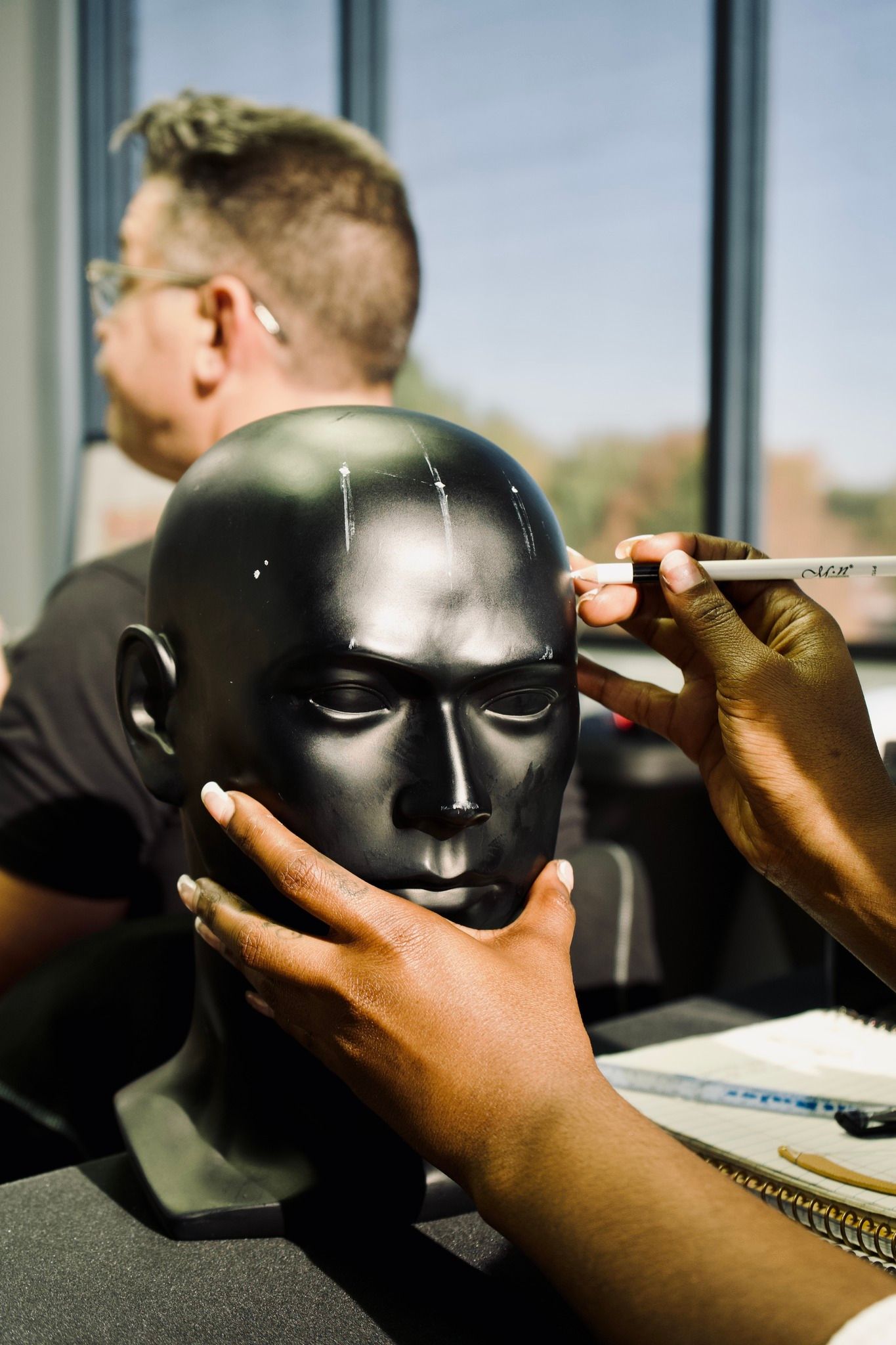 A person is painting a black mannequin head with a marker.