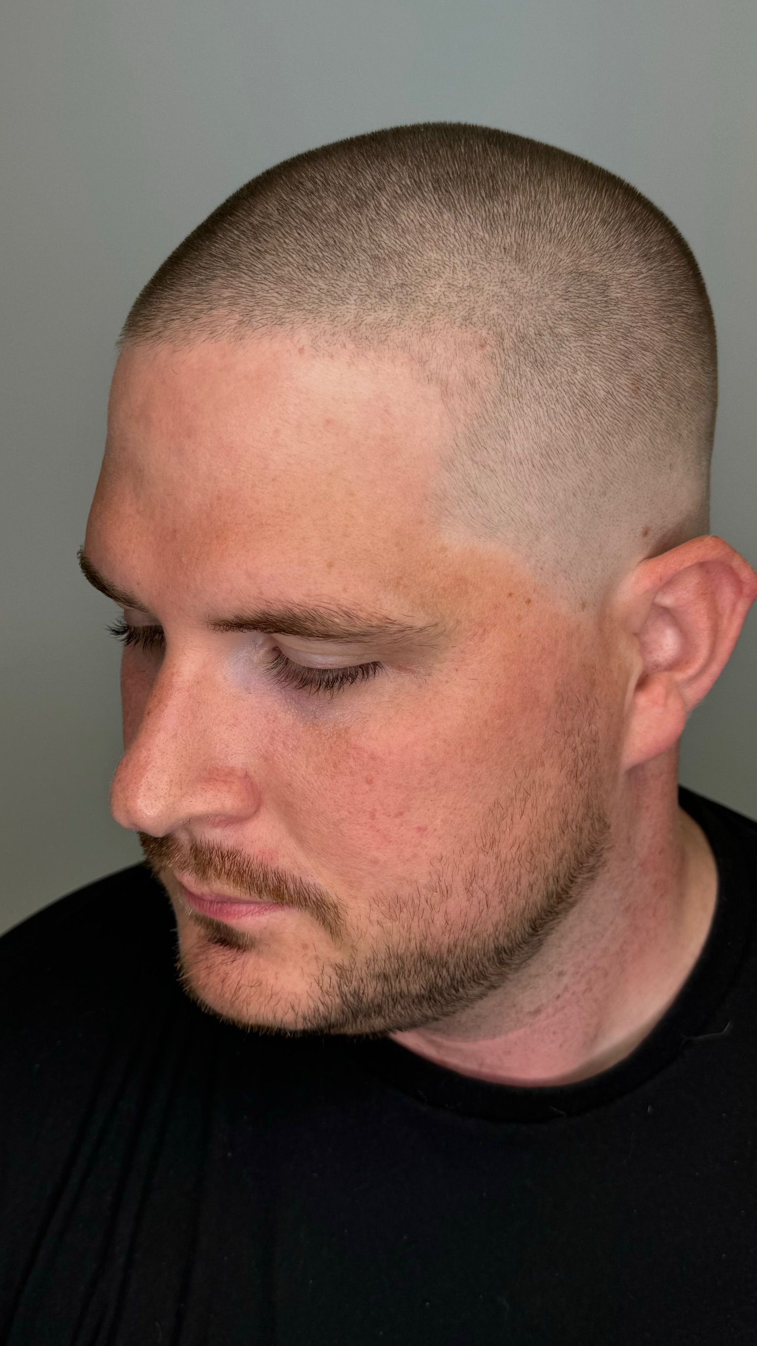 A man with a shaved head and a beard is wearing a black shirt.