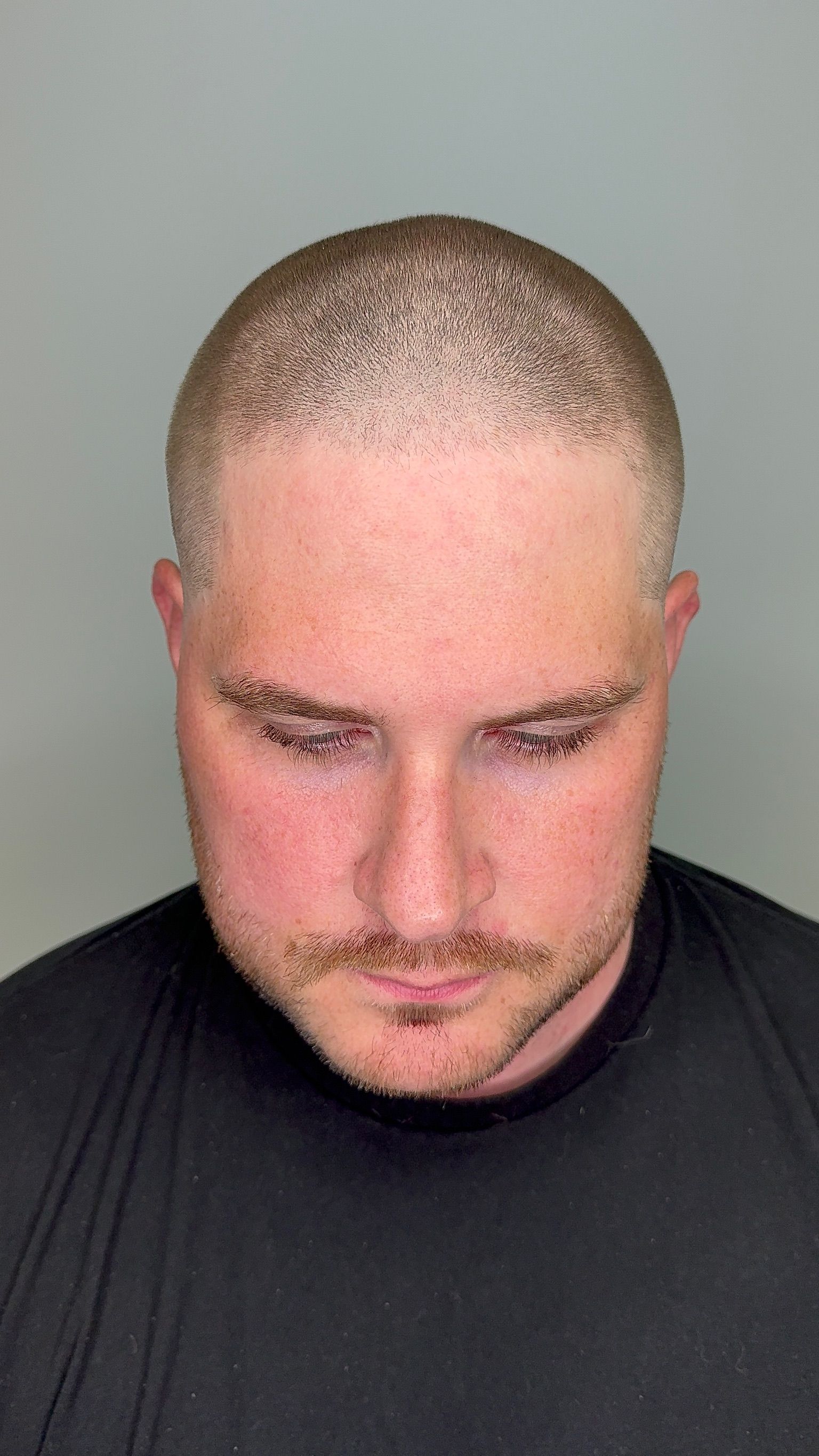 A man with a shaved head and a beard is wearing a black shirt.