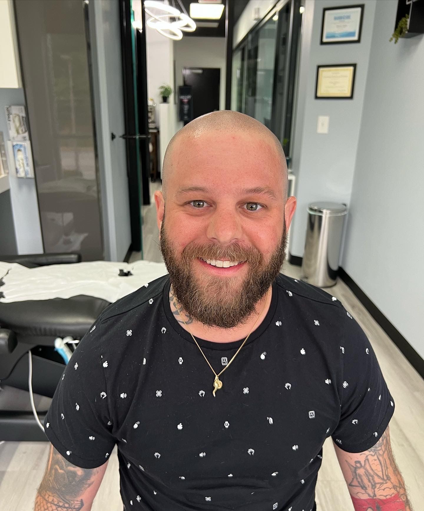 A man with a beard and tattoos is smiling in a room.