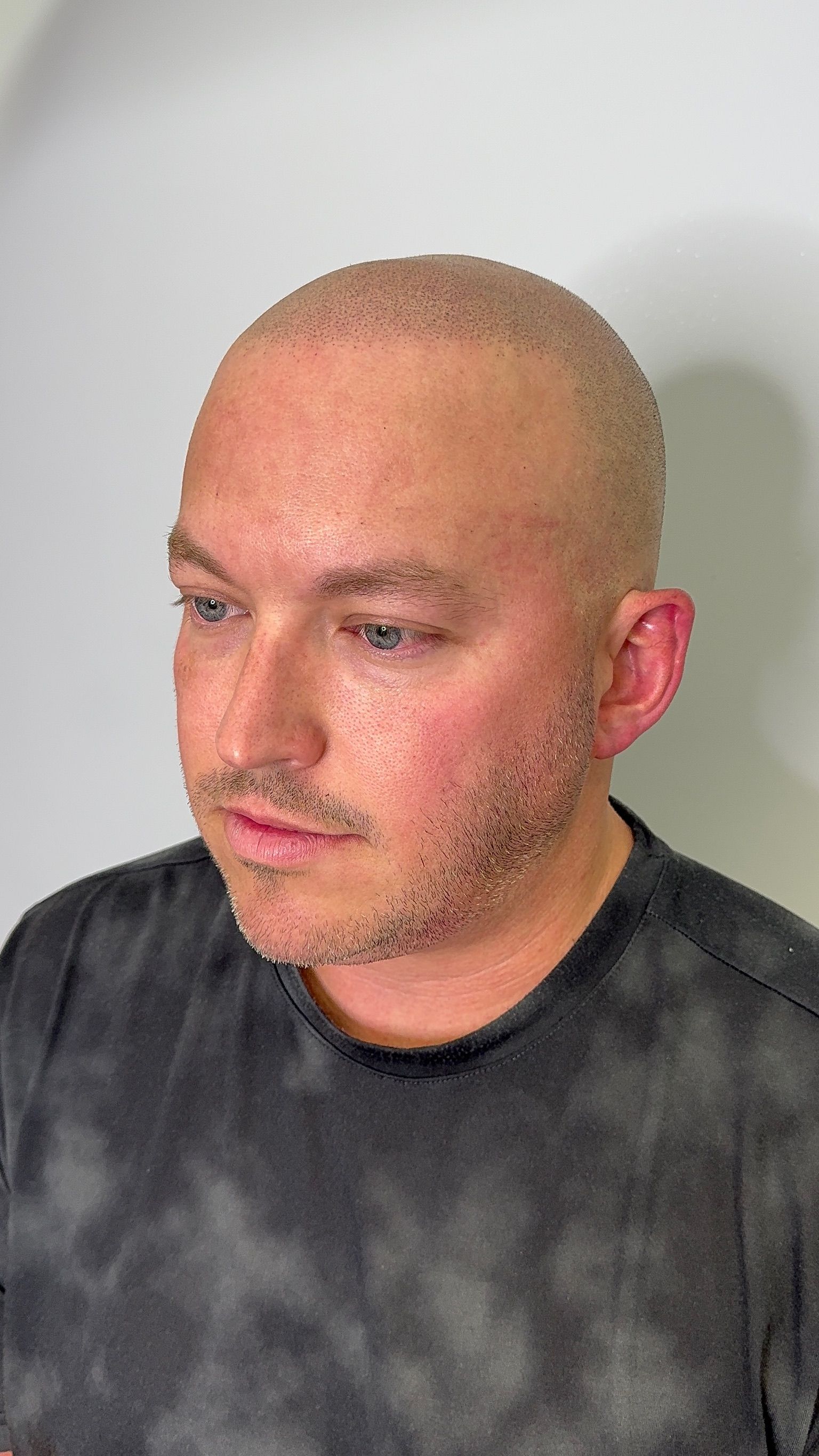 A man with a bald head and a beard is wearing a tie dye shirt.