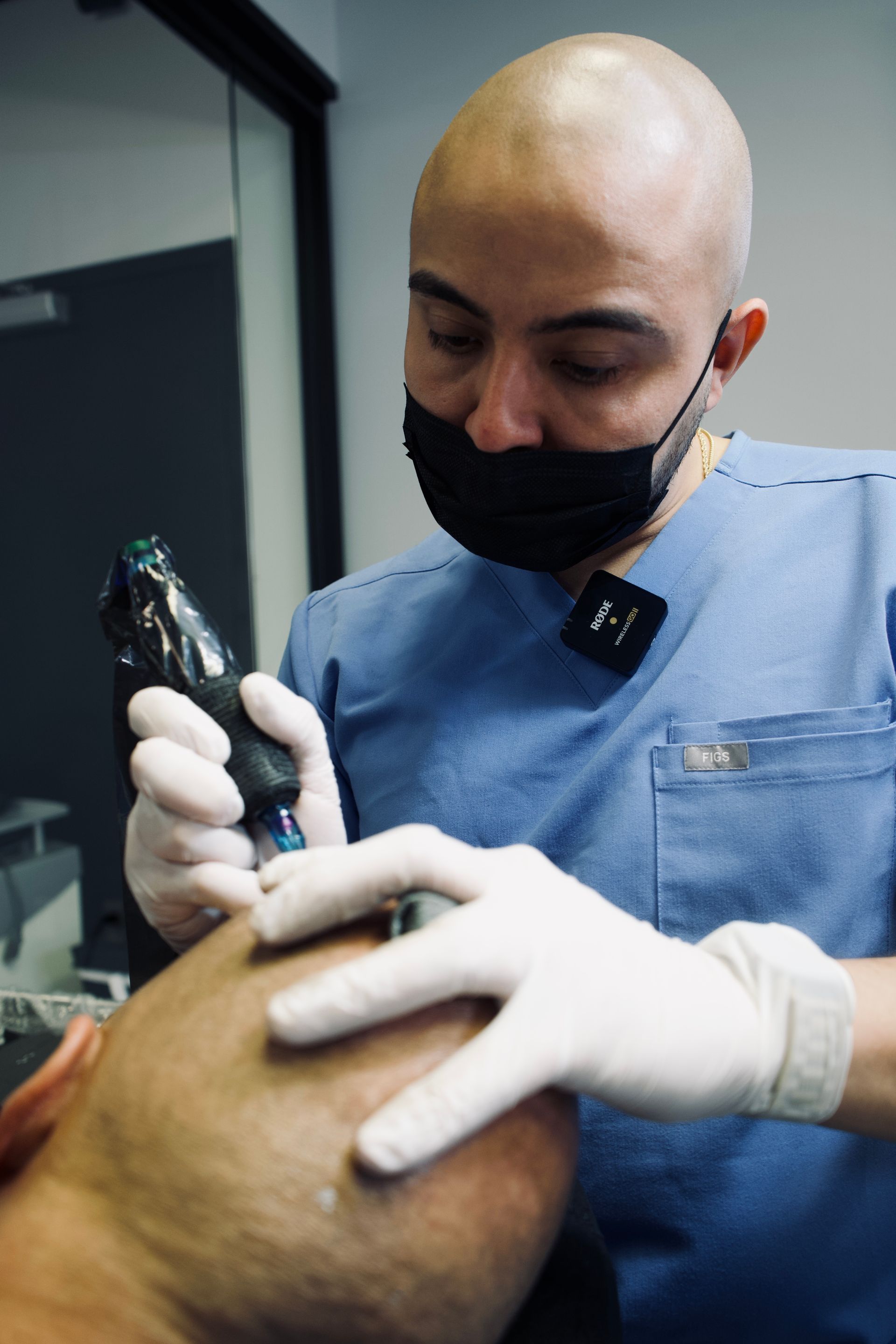 A man wearing a mask and gloves is getting a tattoo on a man 's arm.