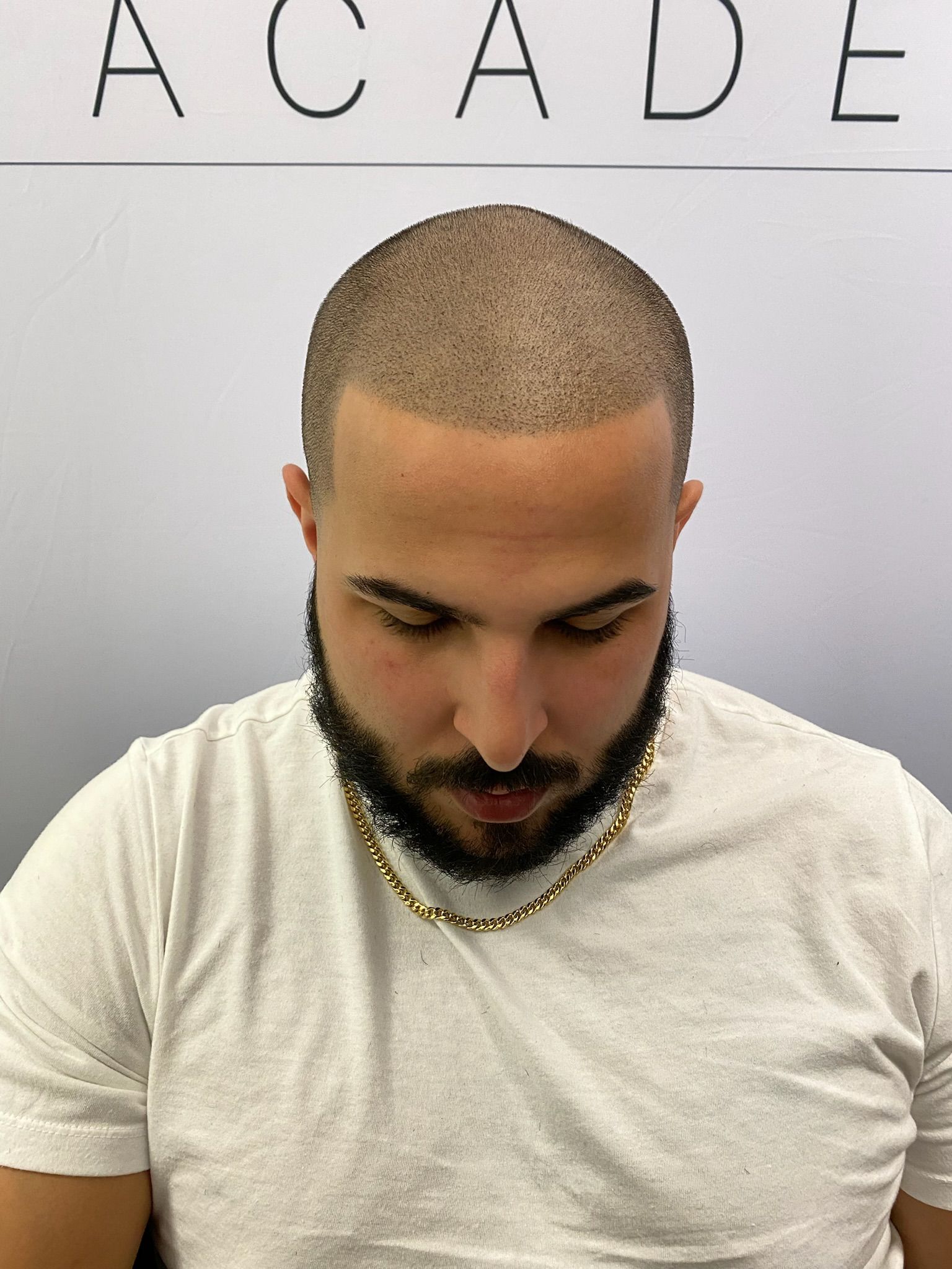 A man with a beard is wearing a white shirt and a gold chain around his neck.