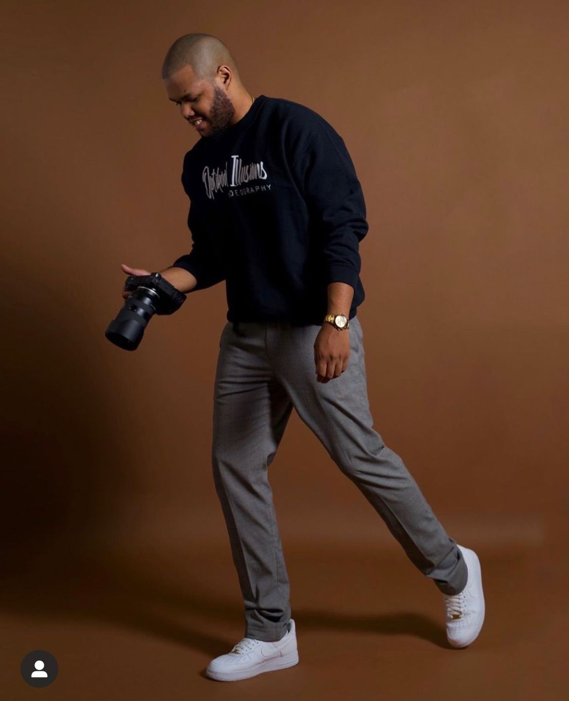 A man wearing a black sweatshirt and grey pants is holding a camera