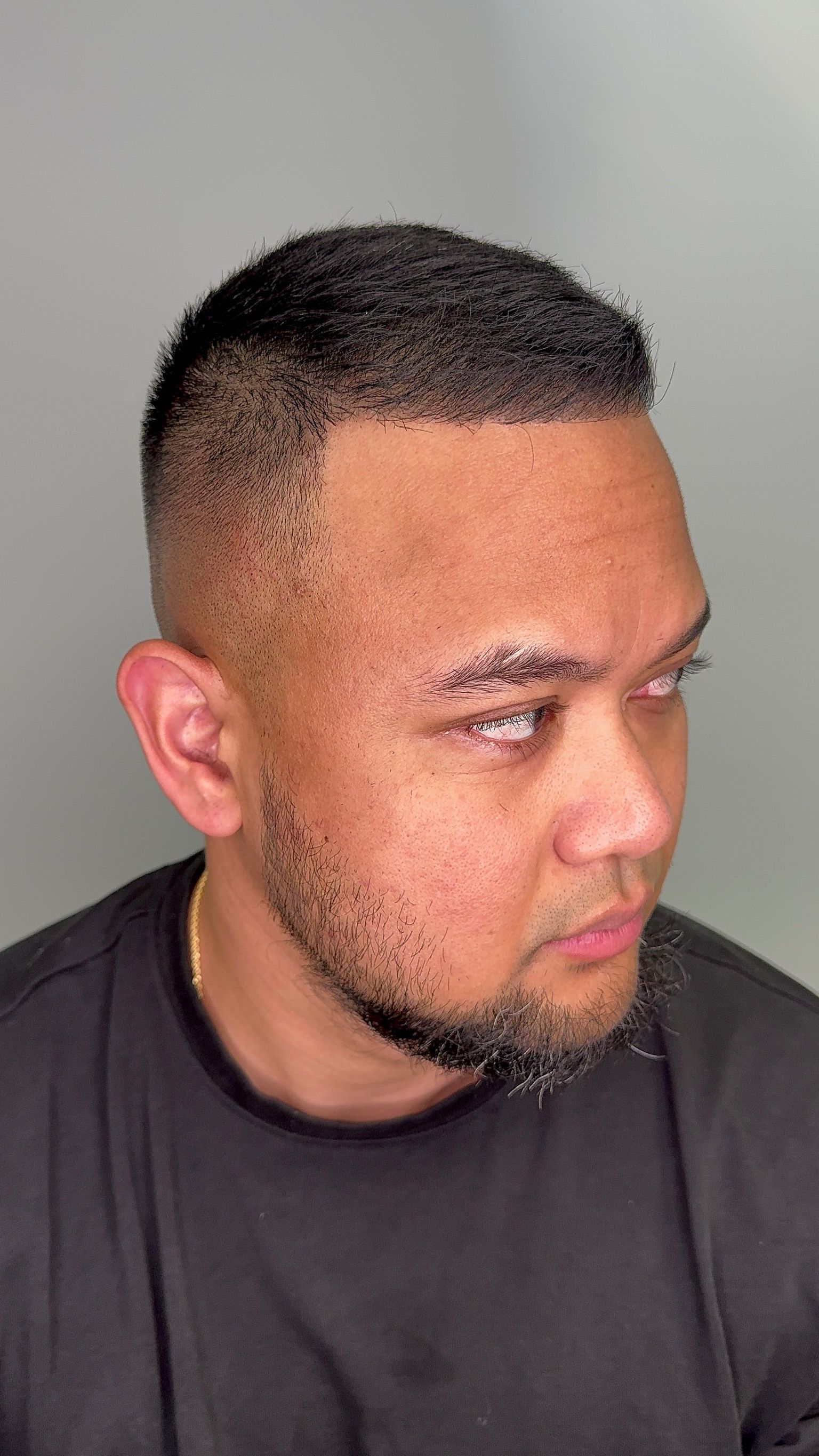 A man with a beard is wearing a black shirt and has a tattoo on his forehead.