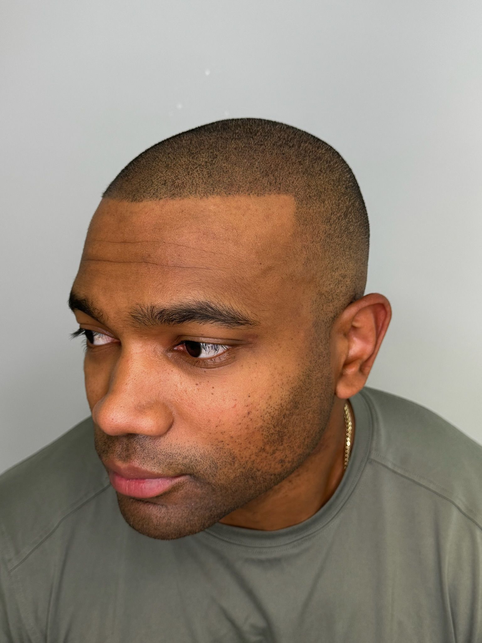 A man with a shaved head and a beard is wearing a green shirt.