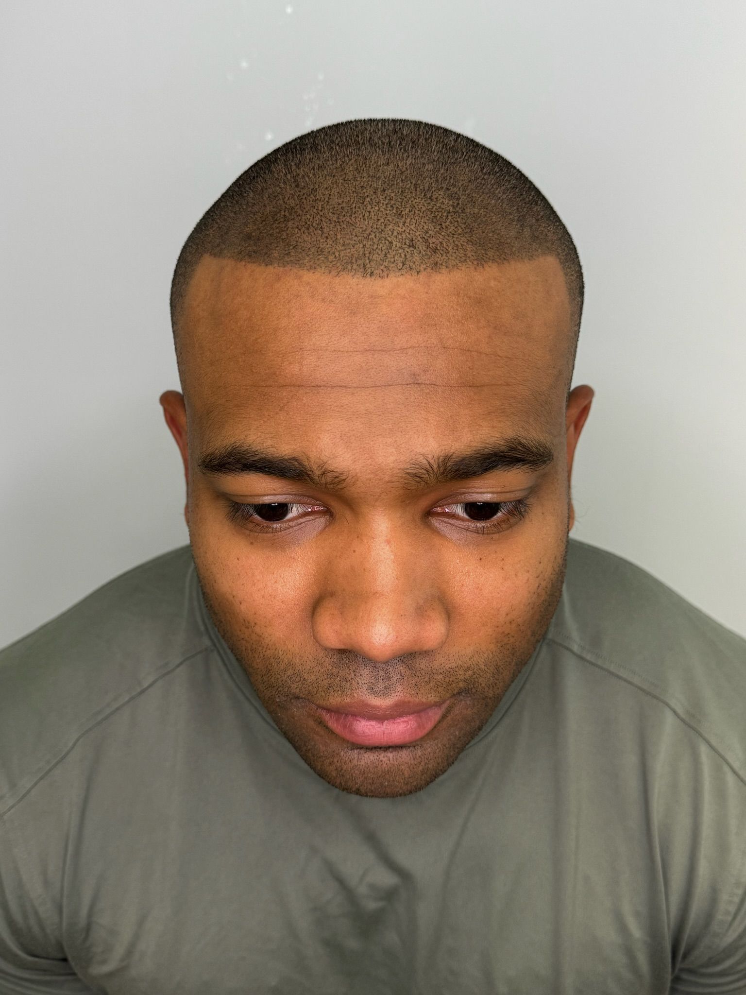 A man with a shaved head and a beard is wearing a green shirt.