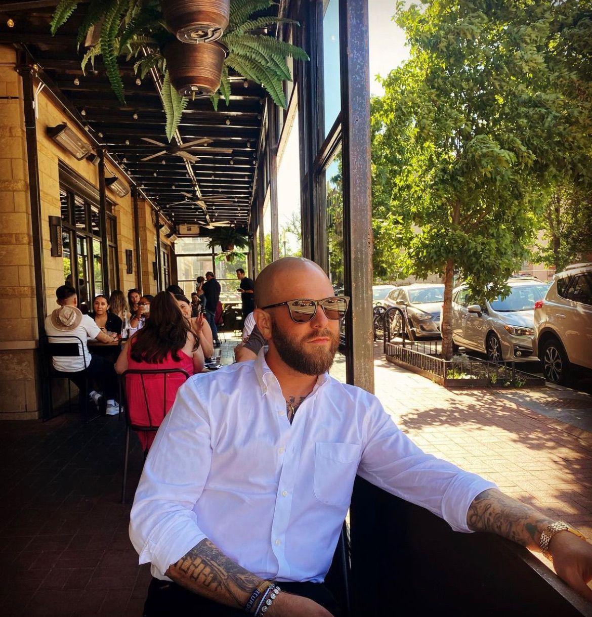 A man wearing sunglasses and a white shirt is sitting outside of a restaurant