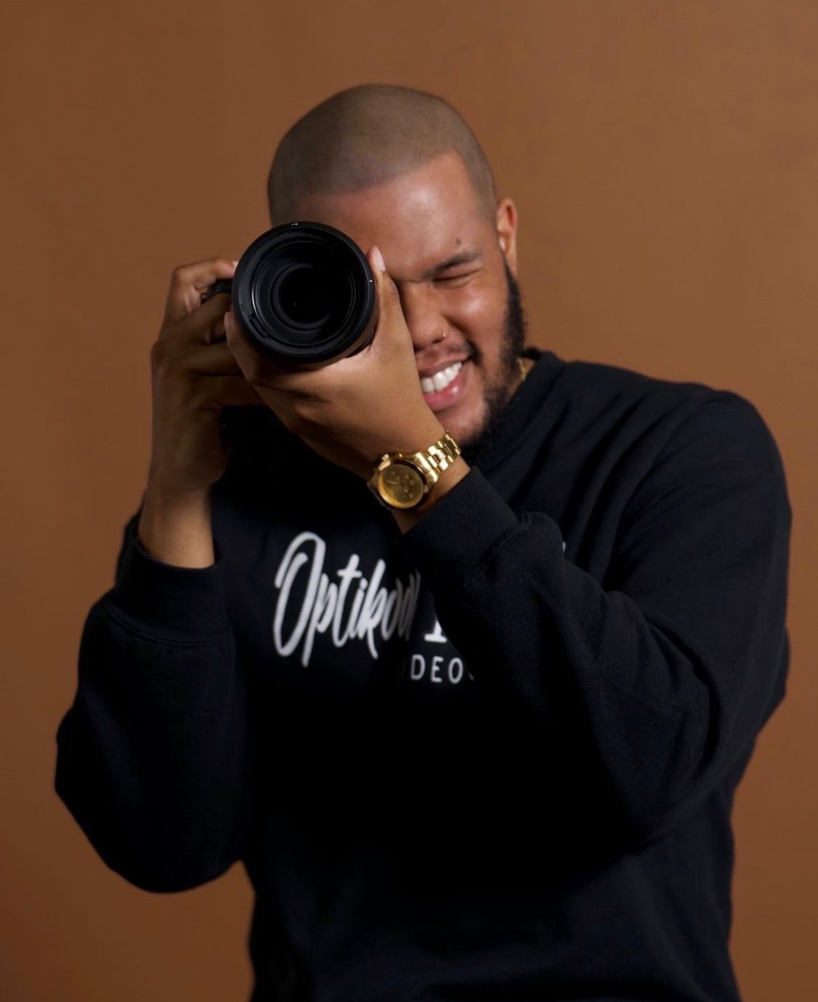 A man wearing a black shirt with the word optik on it is holding a camera