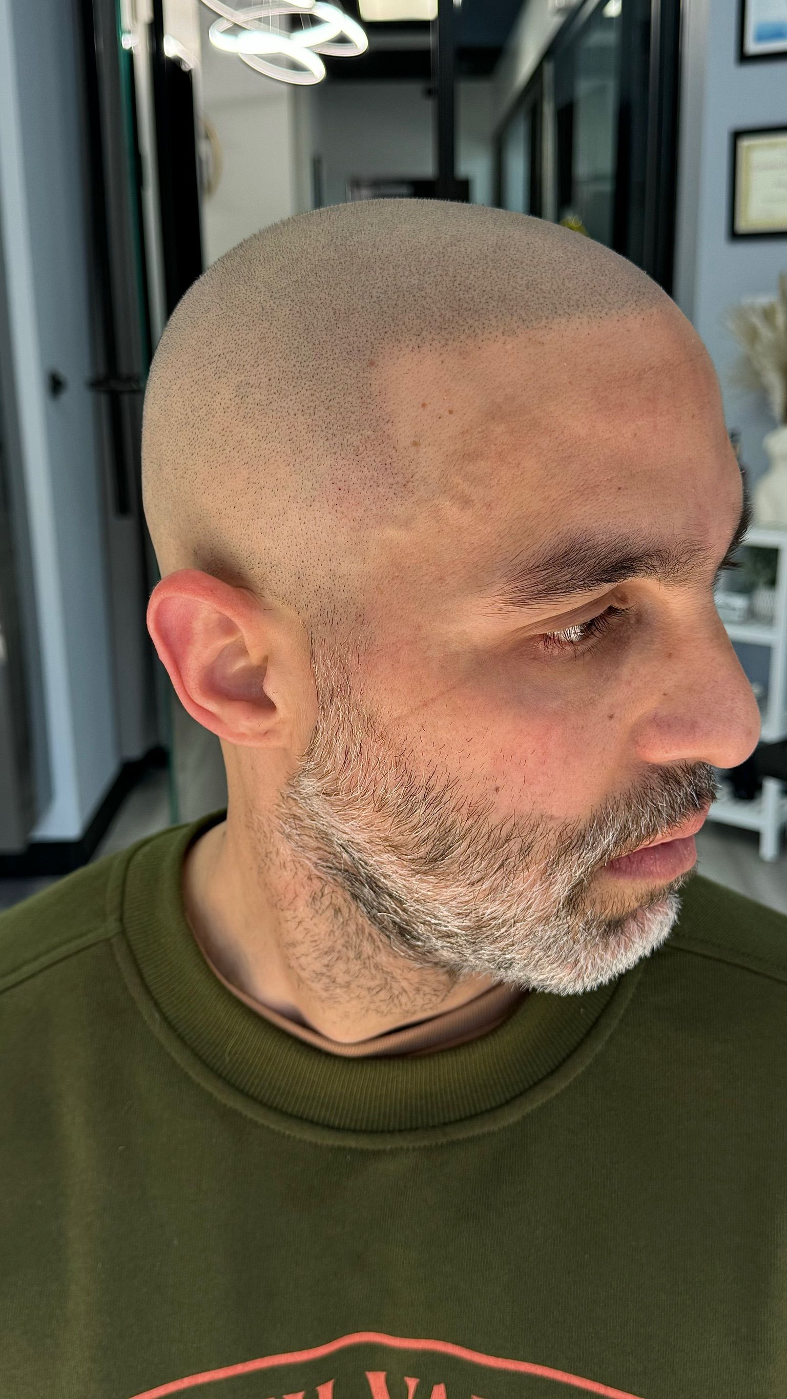 A man with a shaved head and a beard is wearing a green sweater.