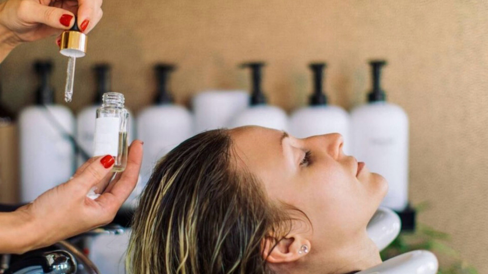 Hairdresser applying serum to client's hair during a salon treatment.