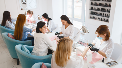 People getting manicures at a nail salon. Technicians wearing masks and black gloves.