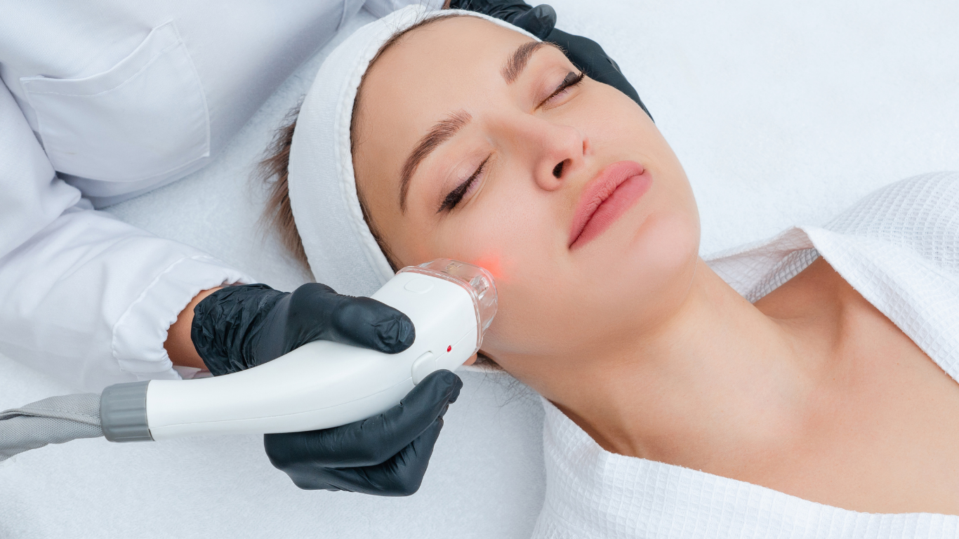 Woman receiving facial laser treatment in a spa setting, with equipment and doctor's hands visible.